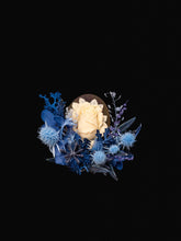 The Camellia Birth Flower Ring by CAMELLIA features a white rose encircled by blue blooms and foliage, beautifully arranged against a solid black background.